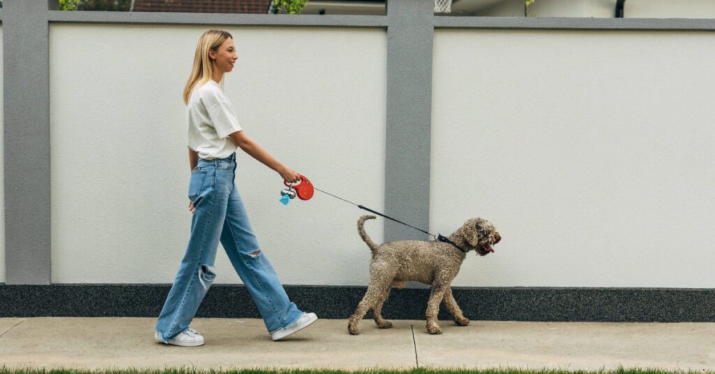 side view of young woman walking her dog on the sidewalk
